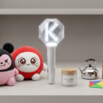 Assortiment d'objets sur une étagère: deux peluches, un lightstick lumineux "K", un pot "K-CARE", une théière, une lettre "K" en bois et un cerf-volant.